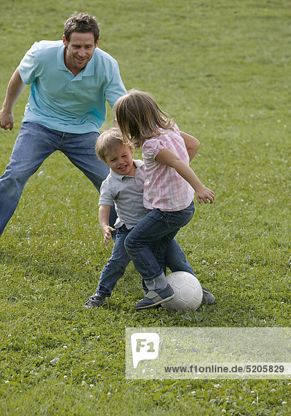 Vater spielt mit zwei Kindern auf Wiese Fußball