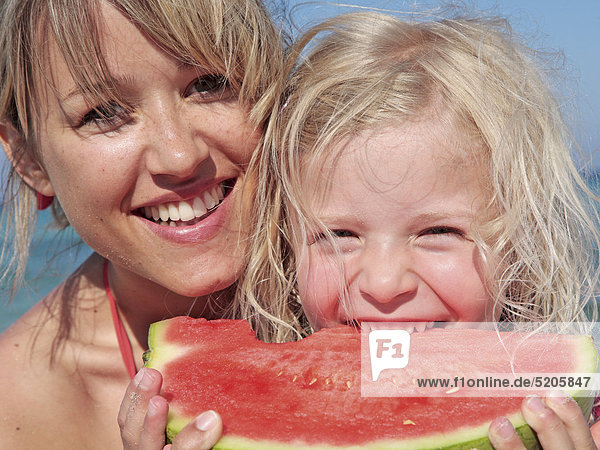 Mutter mit Tochter am Strand  Mädchen beißt in Melone  Porträt