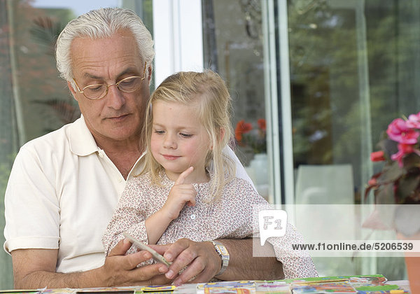 Großvater und Enkelin sitzen auf Terrasse bei Kartenspiel