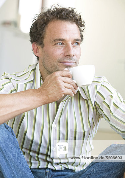 Mann sitzt mit Tasse Kaffee am Boden  Halbporträt