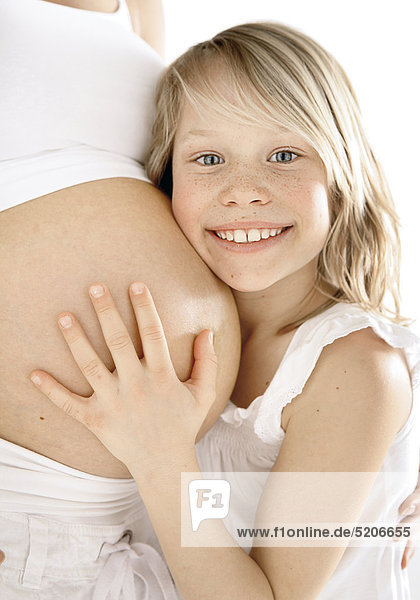 Kleines Mädchen an Bauch von schwangerer Frau gelehnt