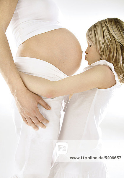 Kleines Mädchen küsst schwangerer Frau auf den Bauch