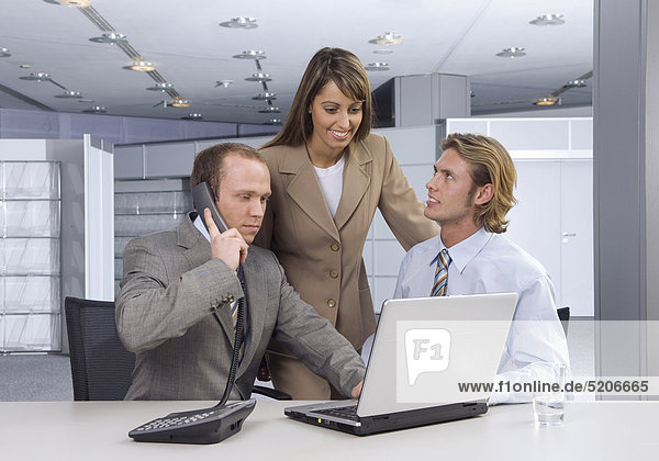 Zwei Männer und eine Frau im Büro an Laptop  einer telefoniert