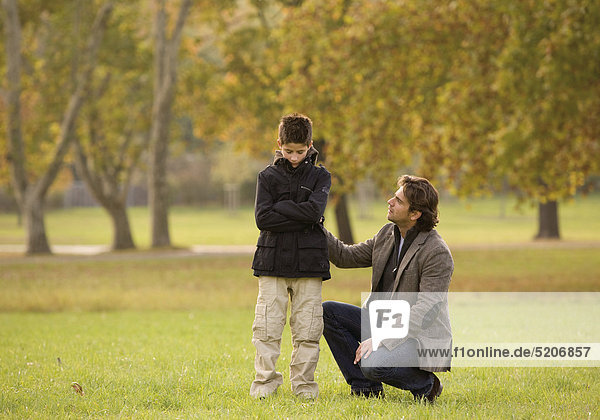 Vater spricht mit verschlossenem Sohn in herbstlichem Park
