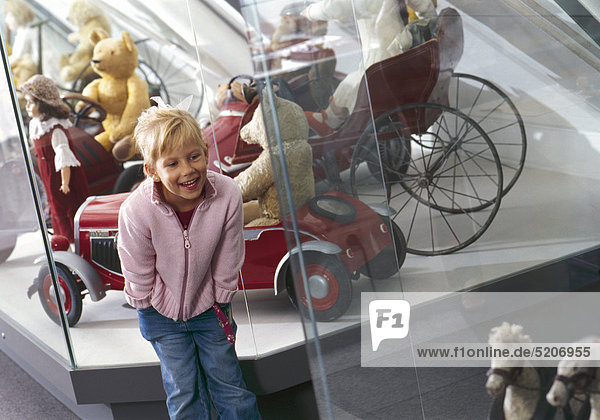 Kleines Mädchen in Spielzeugmuseum  sieht sich Puppen in Vitrine an  lacht