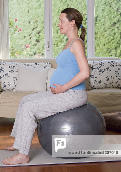 Schwangere sitzt bei Entspannungsübung auf Gymnastikball