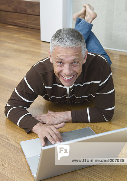 Mann liegt zu Hause mit Laptop am Boden