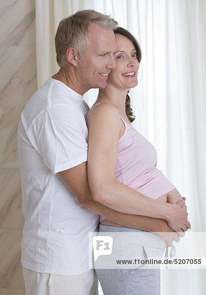 Mann umfasst von hinten den Bauch von schwangerer Frau