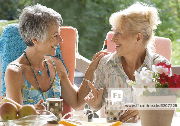 Zwei Seniorinnen sitzen auf Terrasse im Garten  unterhalten sich