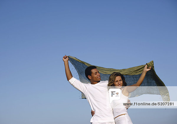 Paar in weißen Shirts mit wehendem Tuch vor blauem Himmel