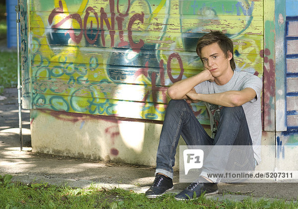 Teenager-Junge sitzt deprimiert an Graffiti-Wand am Boden