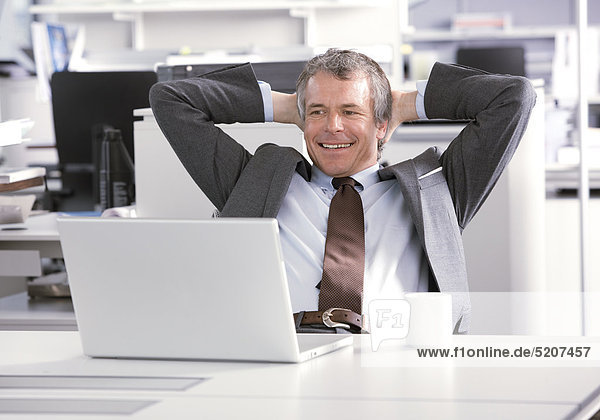 Mann sitzt entspannt im Büro an Laptop  Hände im Nacken