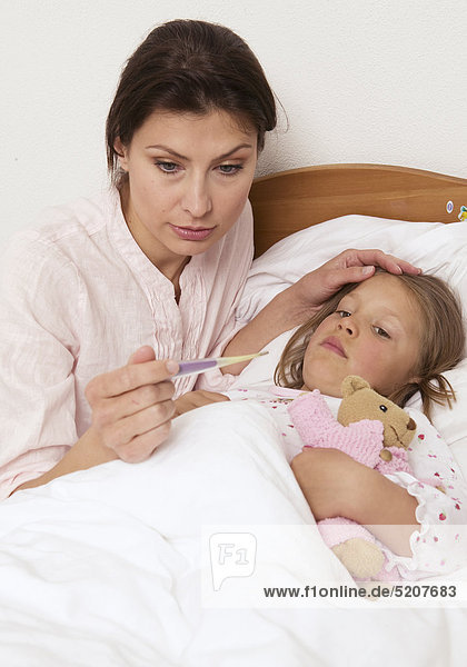 Mutter mit Fieberthermometer bei Tochter am Bett