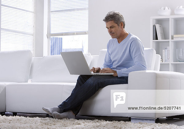 Mann sitzt zu Hause mit Laptop auf Sofa