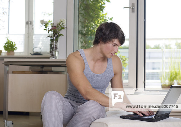 Junger Mann sitzt zu Hause an Laptop