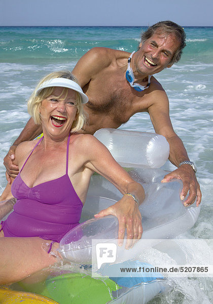 Älteres Paar am Strand mit Schwimmsessel im Wasser