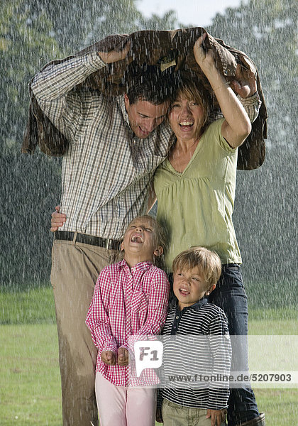 Familie mit zwei Kindern  stehen unter Jacke im Regen