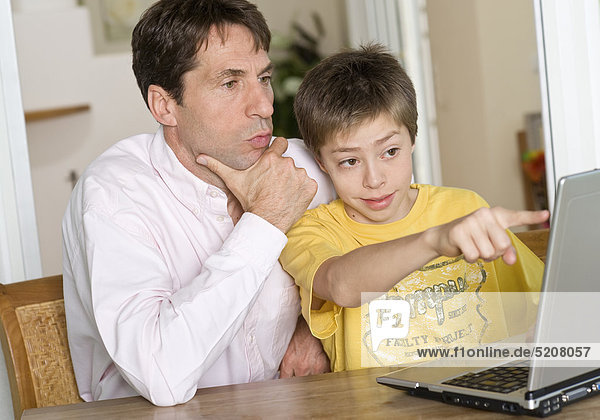 Vater sitzt mit Sohn an Laptop