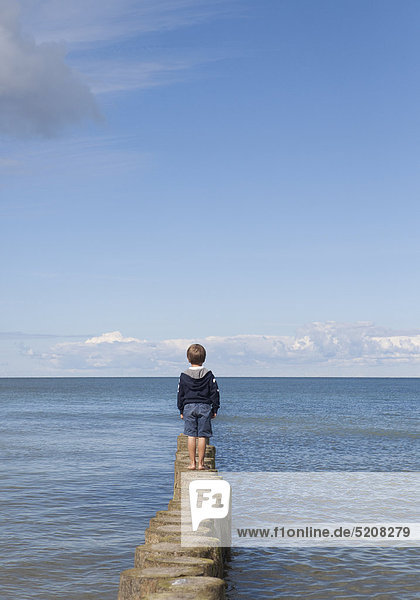 Kleiner Junge steht auf Buhnen am Meer