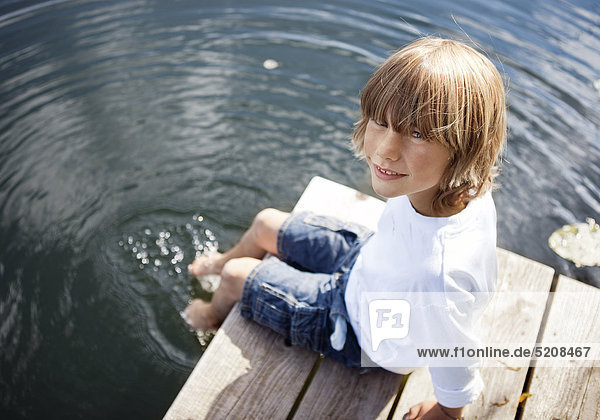 Kleiner Junge sitzt auf Steg und hat die Füße im Wasser