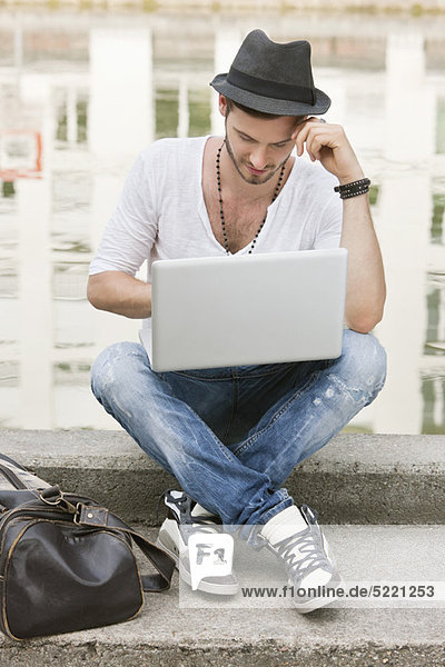 Mann  der auf dem Sims eines Kanals sitzt und einen Laptop benutzt  Paris  Ile-de-France  Frankreich