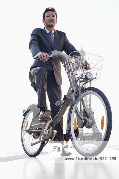 Businessman riding a bicycle with the Eiffel Tower in the background  Paris  Ile-de-France  France