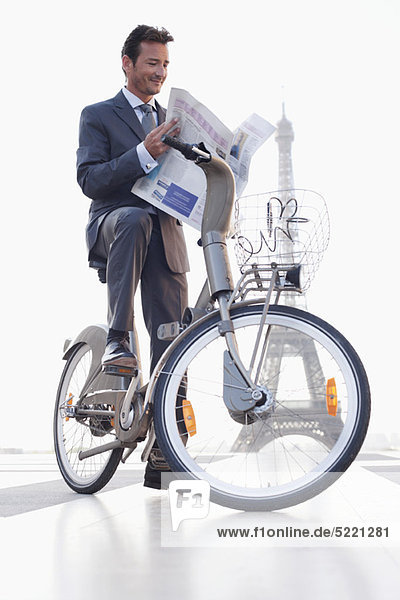 Geschäftsmann beim Lesen einer Zeitung auf einem Fahrrad mit dem Eiffelturm im Hintergrund  Paris  Ile-de-France  Frankreich