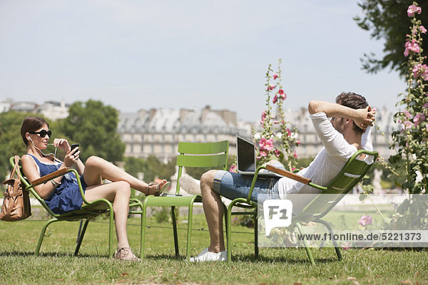 Mann mit einem Laptop und einer Frau auf dem Handy  Jardin des Tuileries  Paris  Ile-de-France  Frankreich