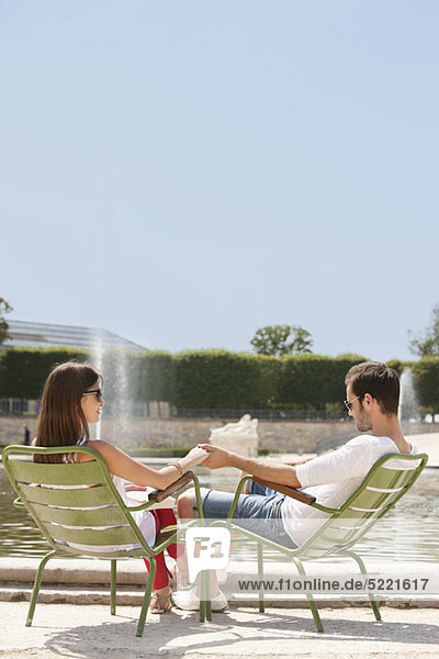 Couple sitting in chairs near a pond,  Bassin octogonal,  Jardin des Tuileries,  Paris,  Ile-de-France,  France