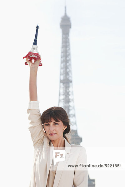 Woman holding a replica of the Eiffel Tower in front of the original one  Paris  Ile-de-France  France