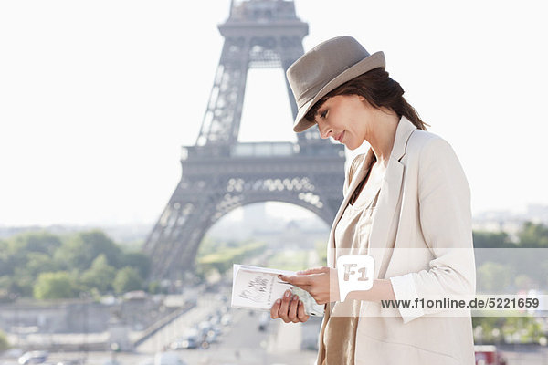 Woman reading a guide book with the Eiffel Tower in the background  Paris  Ile-de-France  France