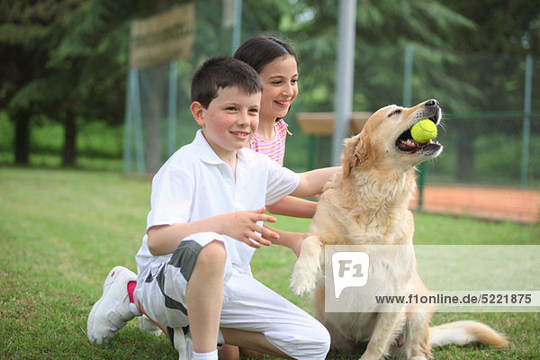 Jungen Jungen und Mädchen spielen mit Labrador Hund Holding Tennisball