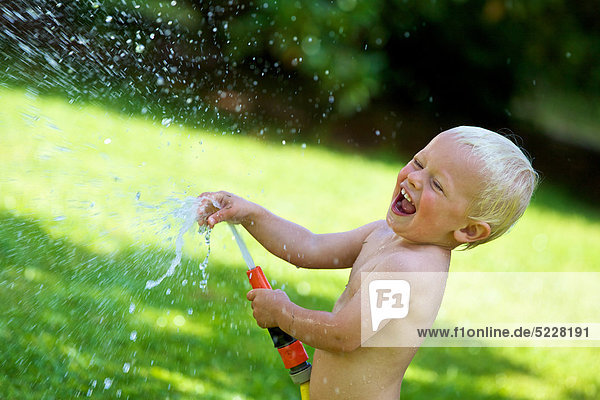 Blond toddler splashing with water in garden