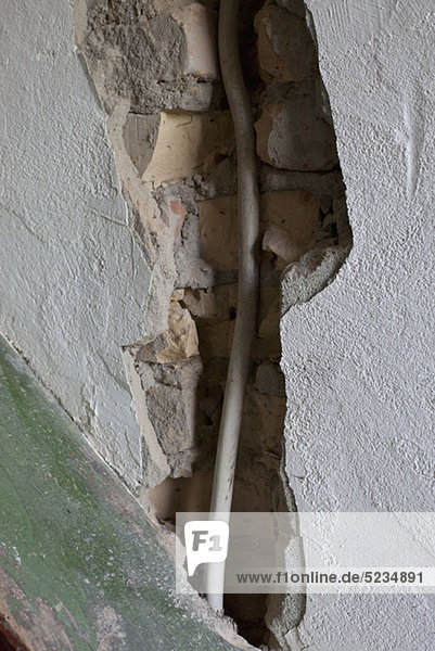 Ein großer Riss in einer Wand  der ein Kabel freilegt.