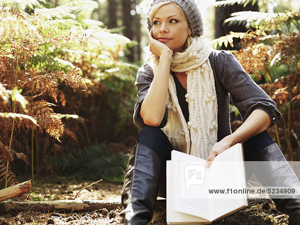A woman in contemplation holding a book  outdoors