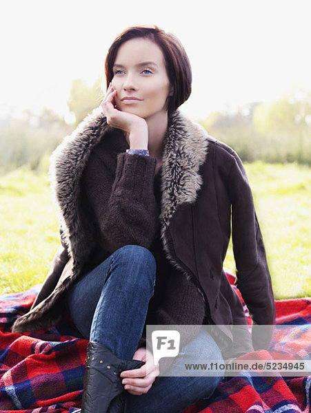 A woman sitting on a blanket and looking away  outdoors