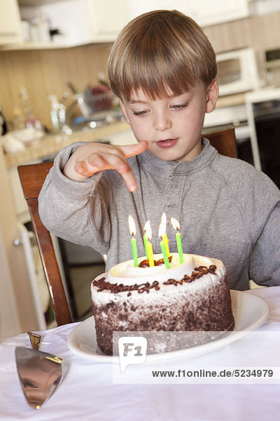 Ein Junge sitzt hinter einem Geburtstagskuchen mit angezündeten Kerzen.