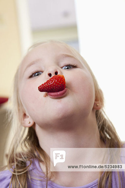 Ein Mädchen mit einer Erdbeere im Mund.