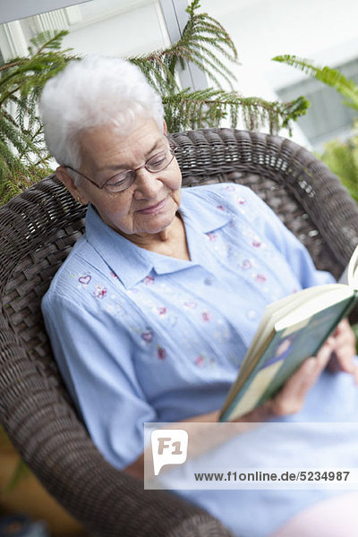 Eine ältere Frau liest in einem Sessel.