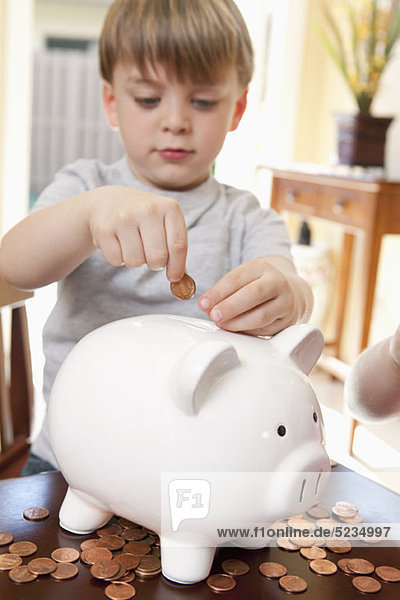 Ein Junge  der Münzen in ein Sparschwein steckt.