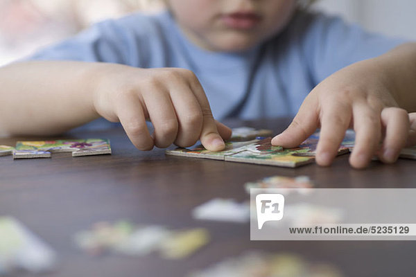 Ein kleiner Junge  der ein Puzzle macht  konzentriert sich auf die Hände.