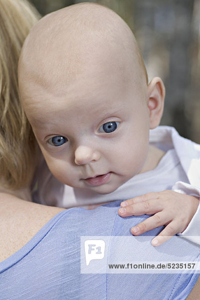 A mother holding a baby  over the shoulder view  focus on baby's face