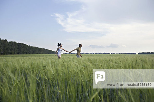 Ein Mann und eine Frau halten sich an den Händen und rennen durch ein Weizenfeld.