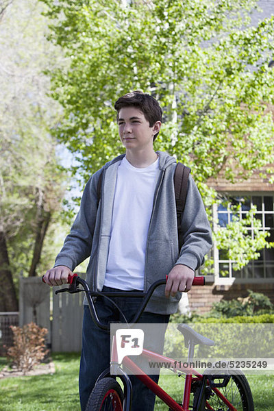 Ein Junge auf dem Rasen hält sein Fahrrad an der Seite.
