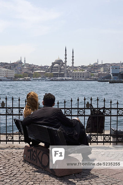 Ein Paar sitzt auf einer Bank mit Blick auf das Goldene Horn bei der Yeni Cami Moschee  Istanbul.