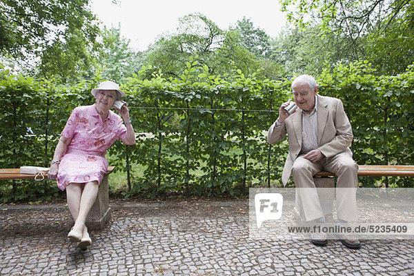 Ältere Männer und Frauen sprechen miteinander auf Blechdosentelefonen im Park.