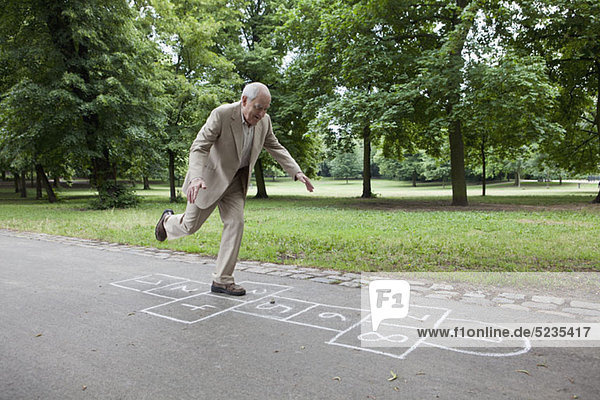 Älterer Mann  der Hopscotch im Park spielt.