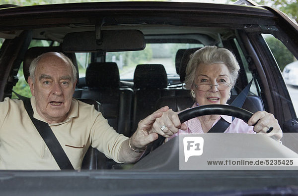 Frau hat Schwierigkeiten beim Fahren  während der Mann im Beifahrer versucht  ihre Hand zu führen.