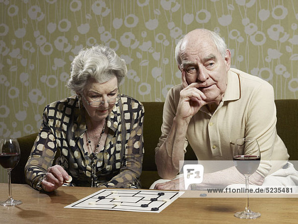 Seniorenpaar spielt Mühle und der Mann sieht ungeduldig aus.