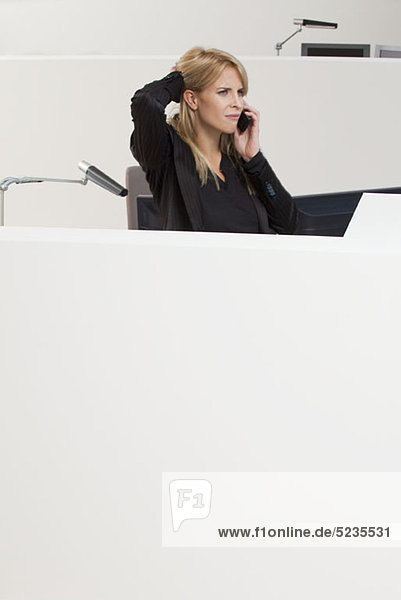 Geschäftsfrau mit Hand am Kopf beim Telefonieren in der Bürozelle